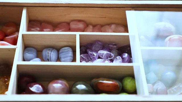  Polychrome jasper, blue agate, amethyst, citrin, rose quartz lie in a wooden box with a transparent lid. The lid of the box opens.