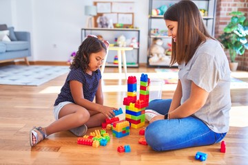 Beautiful teacher and toddler girl playing with construction blocks bulding tower at kindergarten