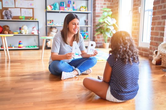 Beautiful teacher teaching alphabet to student toddler girl at kindergarten