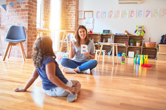 Beautiful teacher teaching alphabet to student toddler girl at kindergarten