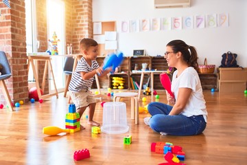 Beautiful teacher and toddler boy playing drum using skitlle and plastic basket at kindergarten
