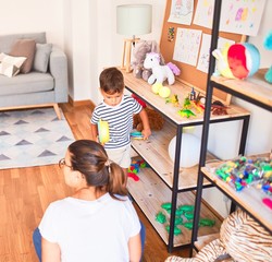 Beautiful toddler boy sitting on puzzle playing with plastic plates, fruits and vegetables at...