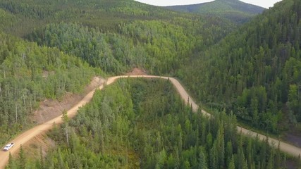 Aerial, drone shot, of a truck car, driving on a dirt road, at the taylor highway, between hills, on a partly sunny day, in Alaska, USA