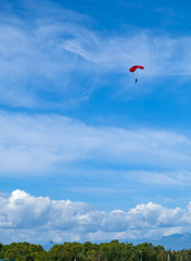Skydiver with a red parachute on the background a blue sky and white clouds. Skydiver above the stormy clouds. Skydive in Spain, Catalunya.