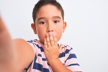 Beautiful kid boy wearing casual striped t-shirt make selfie over isolated white background cover mouth with hand shocked with shame for mistake, expression of fear, scared in silence, secret concept