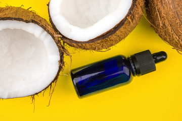 Close up of cracked Coconuts and glass eyedropper bottle isolated on yellow background