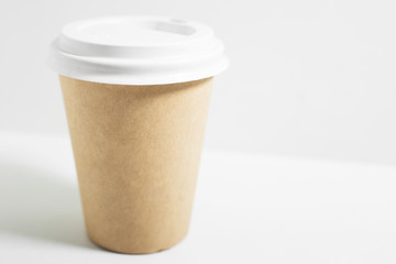 Close-up of disposable paper cup for coffee take away, with white lid, isolated on white background.