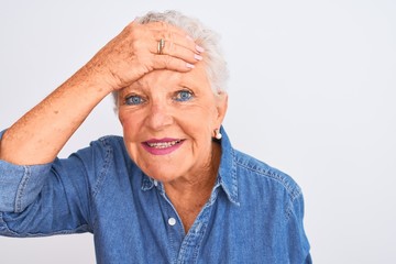 Senior grey-haired woman wearing casual denim shirt standing over isolated white background stressed with hand on head, shocked with shame and surprise face, angry and frustrated. Fear and upset 