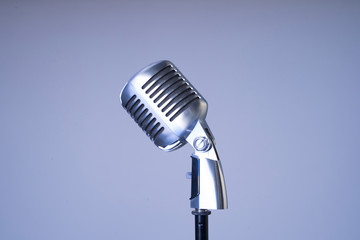 Old style filtered photo of a metallic mic from the side isolated on blue background. Horizontal copy space. Vintage silver microphone closeup on light blue background. Retro oldies music concept.   