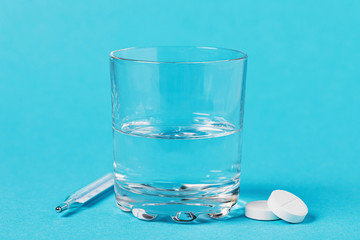 Thermometer, glass of water and pills on a blue background. Concept on the topic of medication