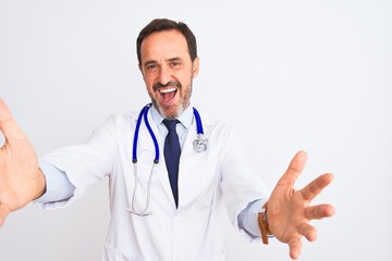 Fototapeta premium Middle age doctor man wearing coat and stethoscope standing over isolated white background looking at the camera smiling with open arms for hug. Cheerful expression embracing happiness.