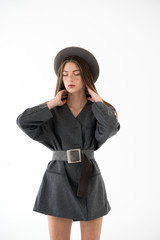 Fototapeta premium Young girl in trench coat with hat on gray background