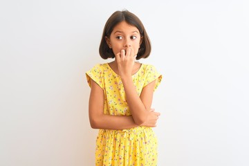 Young beautiful child girl wearing yellow floral dress standing over isolated white background looking stressed and nervous with hands on mouth biting nails. Anxiety problem.