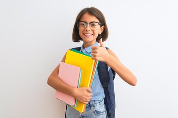Beautiful student child girl wearing backpack glasses books over isolated white background happy with big smile doing ok sign, thumb up with fingers, excellent sign