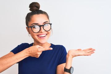 Beautiful woman with bun wearing blue t-shirt and glasses over isolated white background very happy pointing with hand and finger