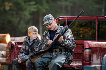 Father and son sitting in a pickup truck after hunting in forest. Dad showing boy mechanism of a...