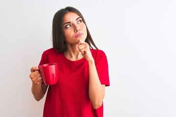 Young beautiful woman drinking red cup of coffee standing over isolated white background serious...