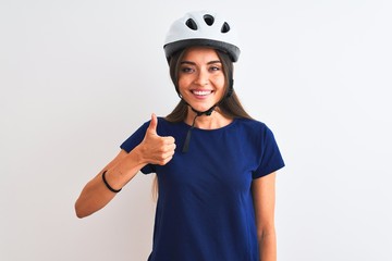 Young beautiful cyclist woman wearing security bike helmet over isolated white background doing happy thumbs up gesture with hand. Approving expression looking at the camera with showing success.
