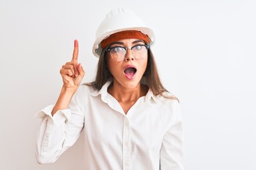 Young beautiful architect woman wearing helmet and glasses over isolated white background pointing finger up with successful idea. Exited and happy. Number one.