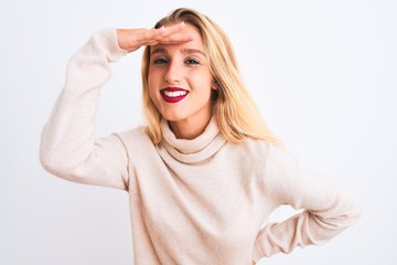 Young beautiful woman wearing turtleneck sweater standing over isolated white background very happy and smiling looking far away with hand over head. Searching concept.