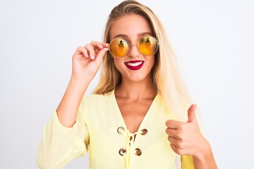 Young beautiful woman wearing yellow t-shirt and sunglasses over isolated white background happy with big smile doing ok sign, thumb up with fingers, excellent sign