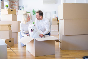 Fototapeta premium Young beautiful couple with dog sitting on the floor at new home around cardboard boxes