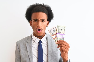 Young african american businessman holding dollars standing over isolated white background scared in shock with a surprise face, afraid and excited with fear expression