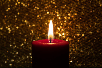One burning red candle  in front of sparkling gold background. Copy space. Christmas decoration. Gold color. Selective focus on candle. Night time.
