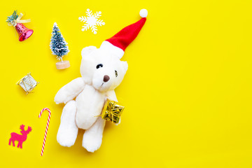 Fototapeta na wymiar Christmas composition, Toy bear wearing a santa hat with gifts, pine tree and decorations on yellow background. Copy space, Christmas holidays concept