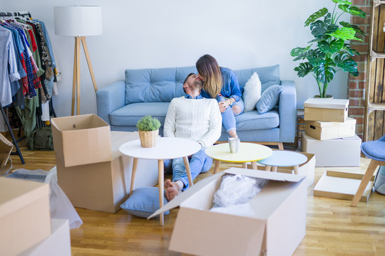 Young beautiful couple sitting on the sofa drinking cup of coffee at new home around cardboard boxes