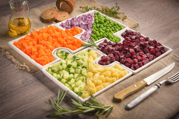 Vegetarian salad. Vegetable salad. Delicious fresh pieces vegetables carrots, cucumber, potatoes, beets and peas close-up with fresh onion. Olive oil on a bag cloth rustic gray table.