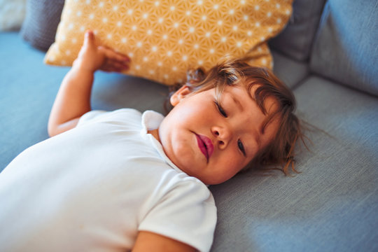 Beautiful toddler child girl wearing white bodysuit lying down on the sofa