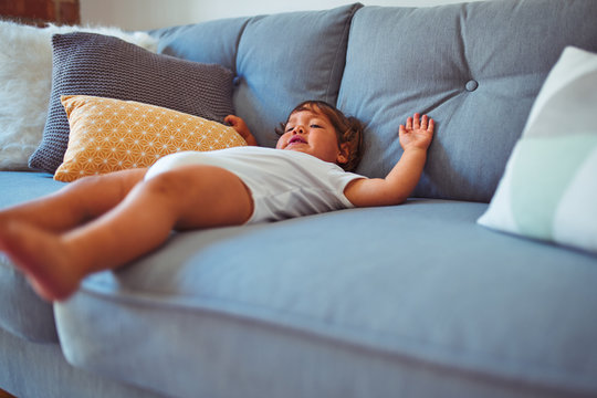 Beautiful toddler child girl wearing white bodysuit lying down on the sofa