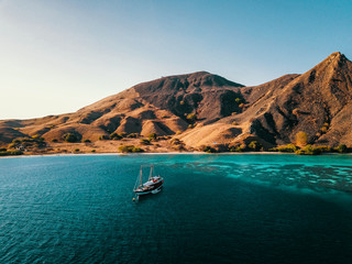 Bird's Eye View of an Dive Boat in front of Komodo Island with visible Reef, Indonesia. Liveaboard Drone Shot.