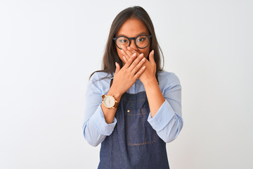 Young beautiful chinese woman wearing glasses and apron over isolated white background shocked covering mouth with hands for mistake. Secret concept.