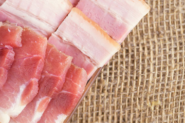 Raw chopped bacon for cooking. Fresh cold sliced bacon on the background of natural linen fabric. Raw chopped bacon for cooking.