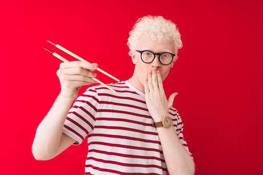 Young albino blond man holding chopsticks standing over isolated white background cover mouth with hand shocked with shame for mistake, expression of fear, scared in silence, secret concept