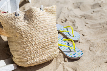 Beach sandals and beach bag lie on the sand on the beach with waves
