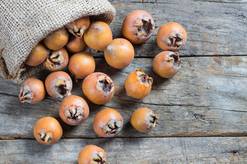 Fresh ripe organic common medlar fruit in burlap sack on wooden rustic background. Healthy food Mespilus germanica