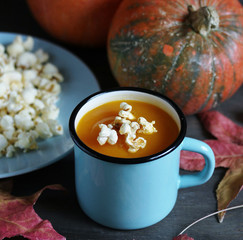 pumpkin soup with popcorn  in an enamel mug on a dark background.