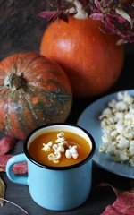 pumpkin soup with popcorn  in an enamel mug on a dark background.