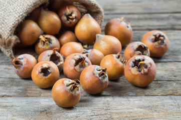 Fresh ripe organic common medlar fruit in burlap sack on wooden rustic background. Healthy food Mespilus germanica