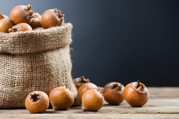 Fresh ripe organic common medlar fruit in burlap sack on grey rustic background. Healthy food Mespilus germanica