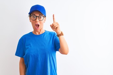 Senior deliverywoman wearing cap and glasses standing over isolated white background pointing finger up with successful idea. Exited and happy. Number one.