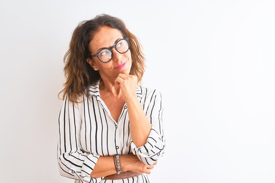 Middle age businesswoman wearing striped dress and glasses over isolated white background with hand on chin thinking about question, pensive expression. Smiling with thoughtful face. Doubt concept.