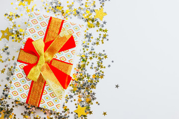 Gift box and stars confetti on white table, top view. Flat lay composition for Christmas or New Year