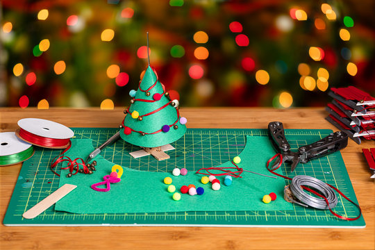 A crafting workspace with materials and tools for making the construction paper Christmas tree and decorations.  There is ample negative space for copywriting on the heavy bokeh background.