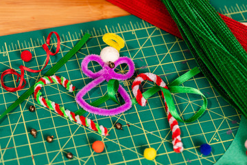 Holiday pipe cleaner crafts. A tight framed Angel and Candy Canes made of pipe cleaners, with additional supplies scattered around the finished crafts on a green cutting mat.