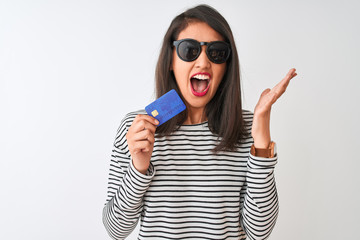 Young chinese woman wearing sunglasses holding credit card over isolated white background very happy and excited, winner expression celebrating victory screaming with big smile and raised hands