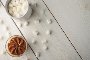 Tiramisu two glasses with marshmallows and a cup of coffee on a light wooden background